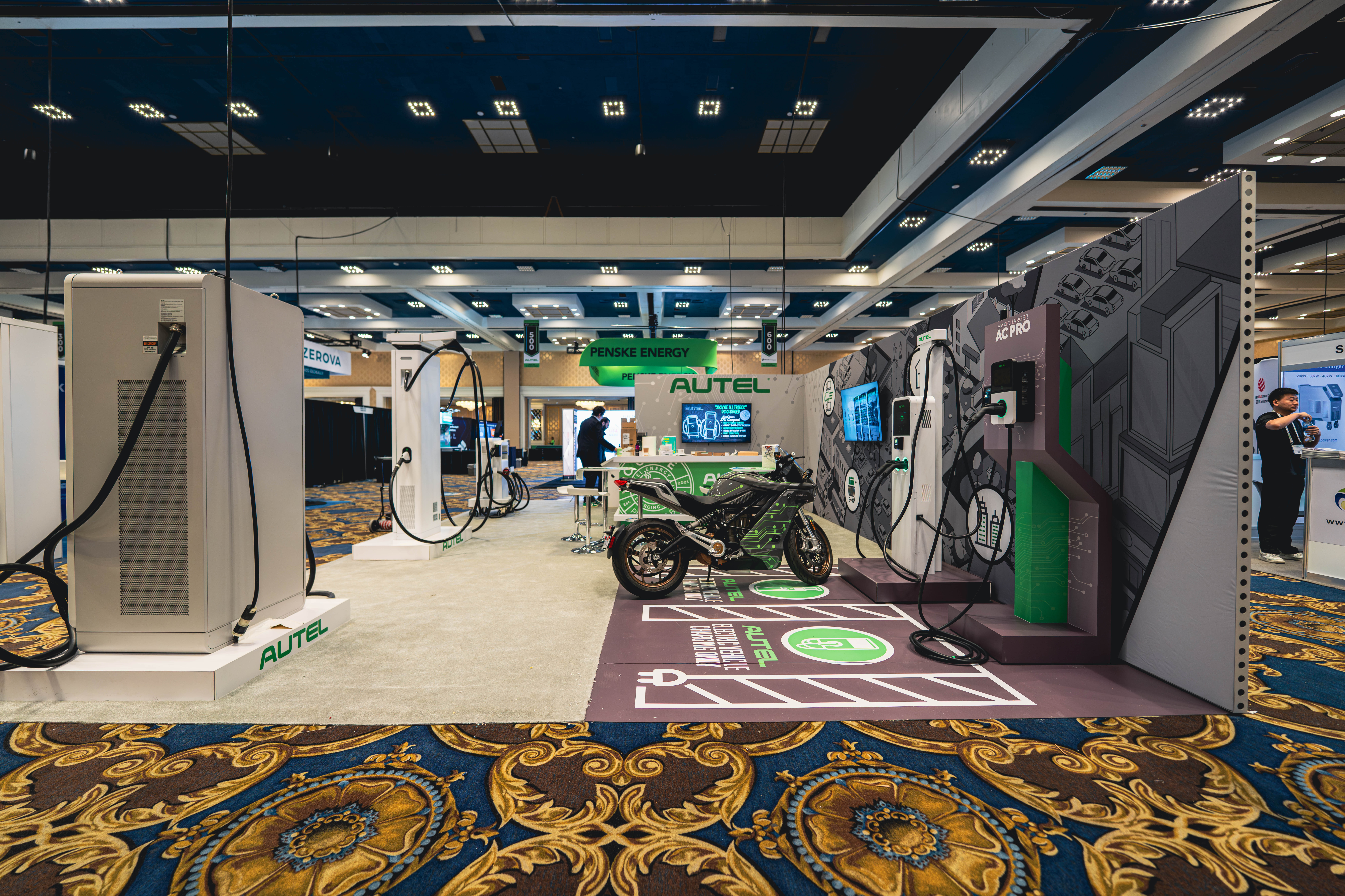 Wide view of Autel’s 20×30 booth at EV Summit with custom charging displays, motorcycle demo, and branded café zone by Disciple Built